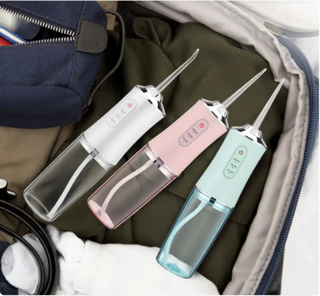 Three electric toothbrushes in white, pink, and blue on a travel bag background.